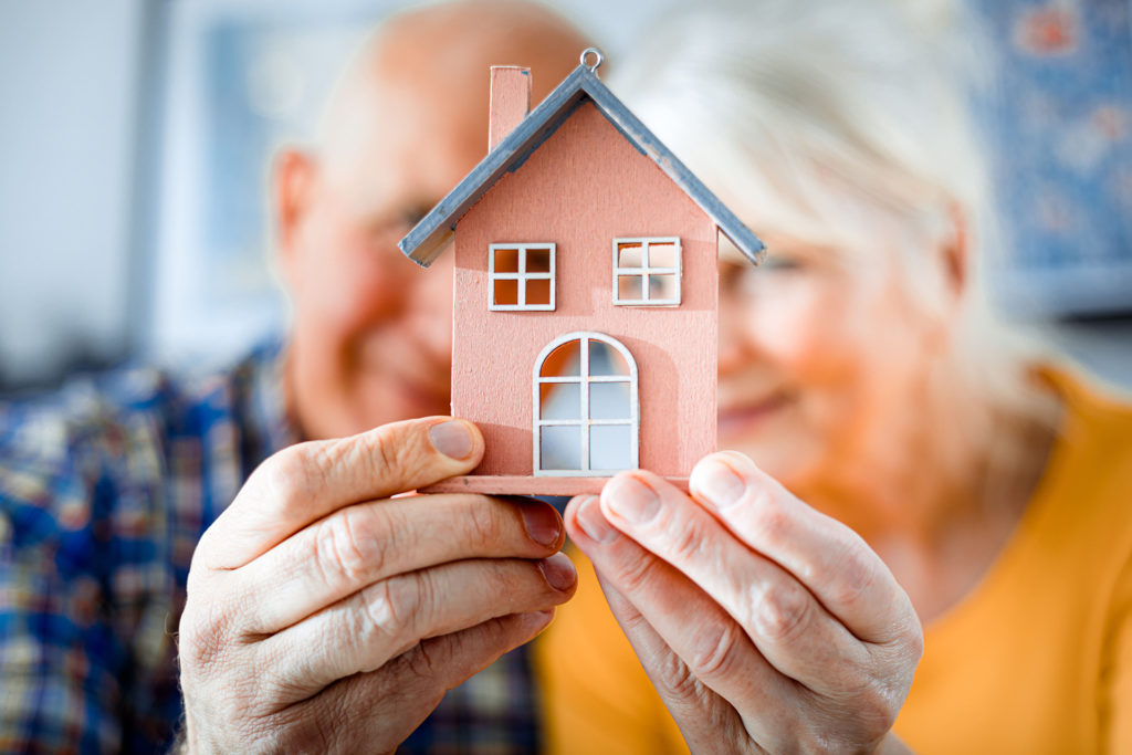 Elderly couple hold a house-shaped ornament up to the camera