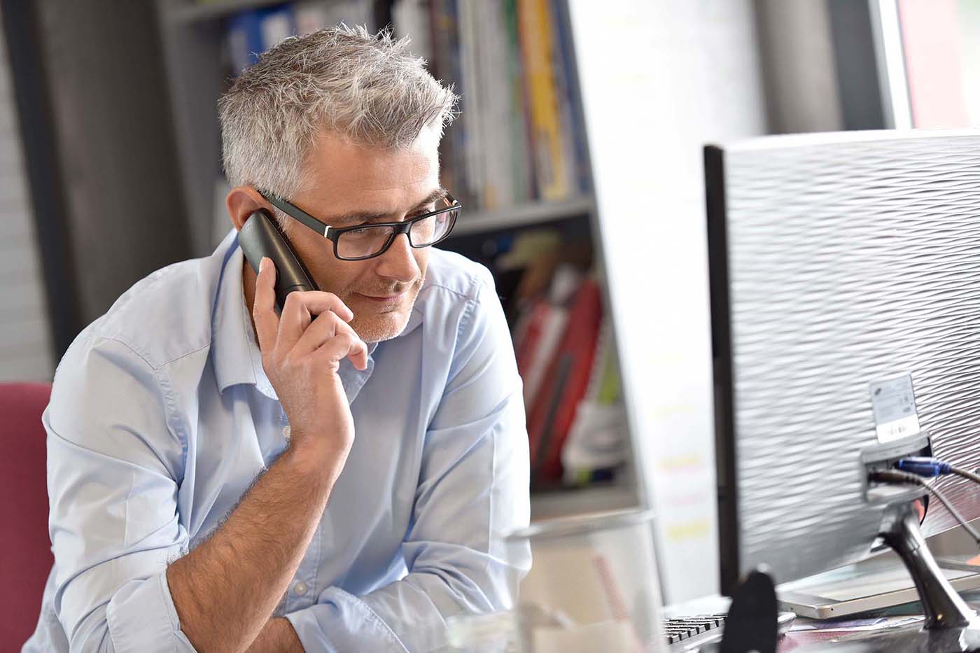 Middle-aged man sits at desk, talking on phone with a financial coach