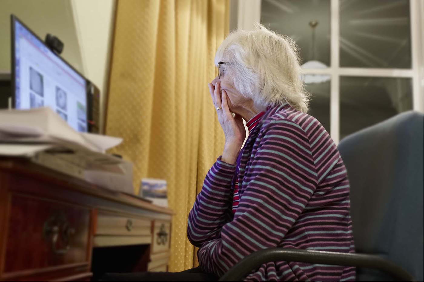 Older woman looks at screen with hand to mouth, very concerned.