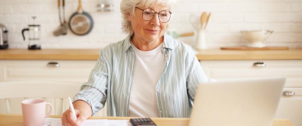 Older woman reviewing bills and looking for information online.