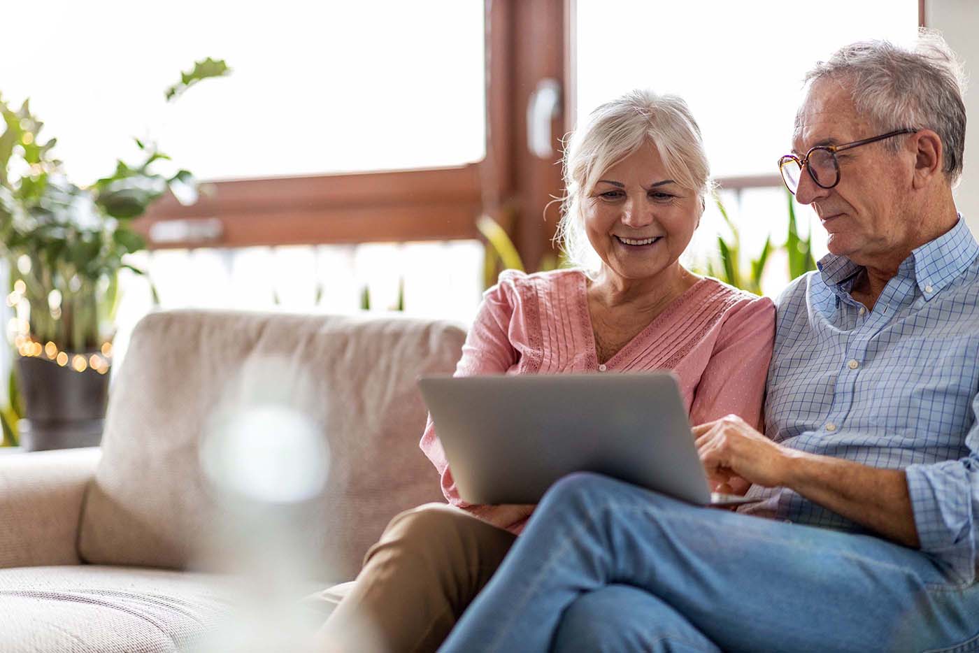 Older couple sitting comfortably on their couch, browsing website on a shared laptop